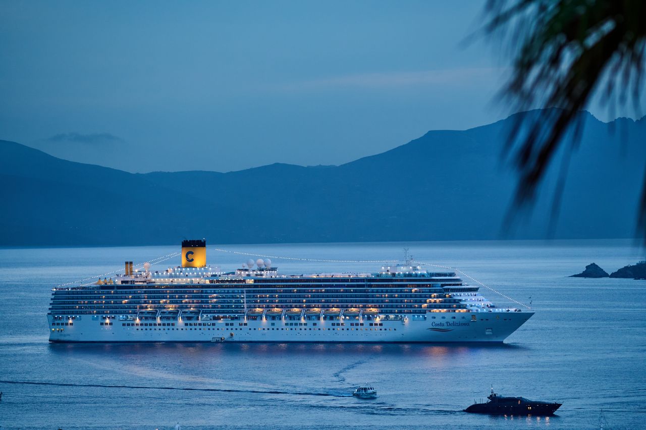 about-us-01 A beautifully illuminated cruise ship sails across the calm sea at dusk, framed by mountains.